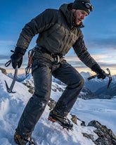 Person ice climbing on a snowy mountain with crampons and ice axes.