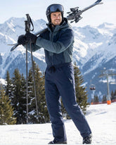 Man in ski gear with skis and poles against a snowy mountain background