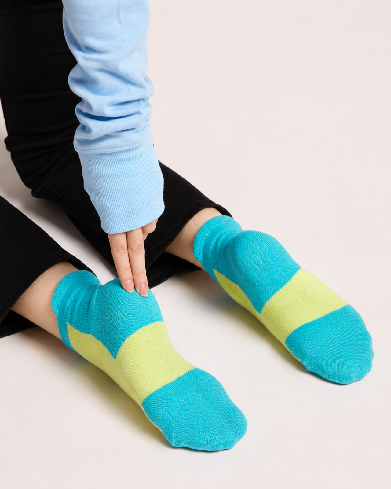 A person wearing neon green quarter socks, with one hand adjusting the sock on the left foot against a plain light background.