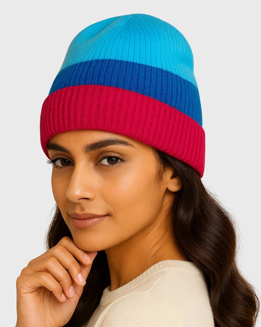 Woman in a striped blue and red knit beanie, cream sweater, and soft makeup, posing with hand near chin.