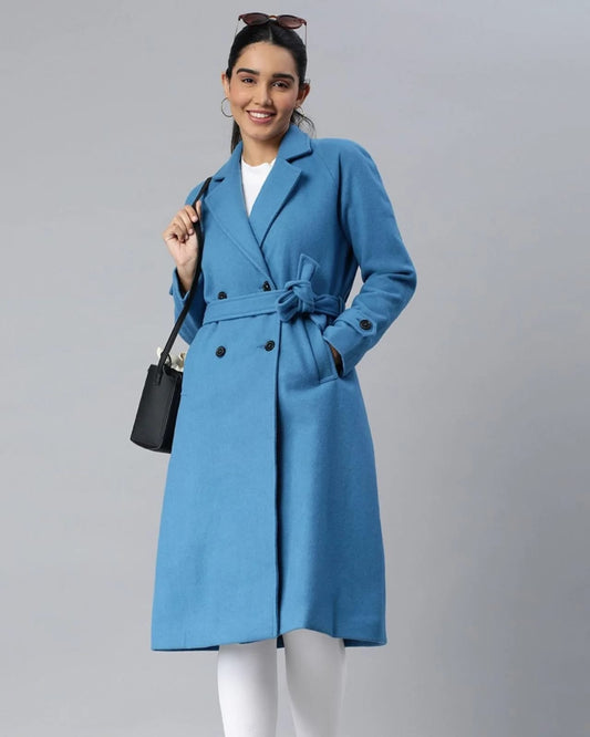 Woman wearing a stylish navy blue double-breasted winter coat with a waist belt, posing confidently for Kosha's winterwear.