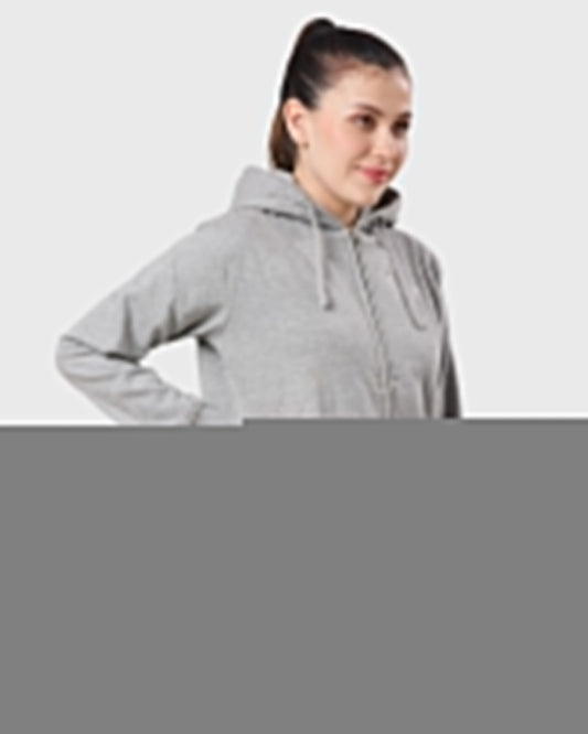 A woman in a gray zip-up hoodie with her hand in the pocket, standing against a light gray background. She is smiling, conveying a relaxed and casual vibe.