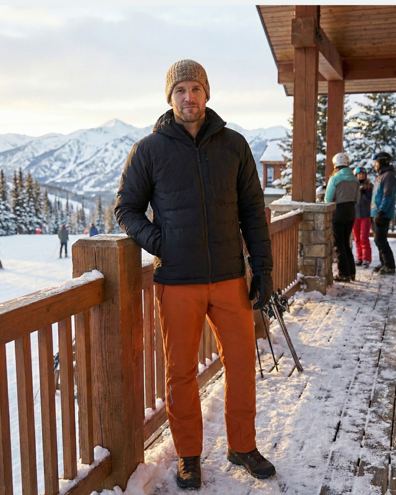 Man in winter clothing standing on a snowy deck with mountains in the background