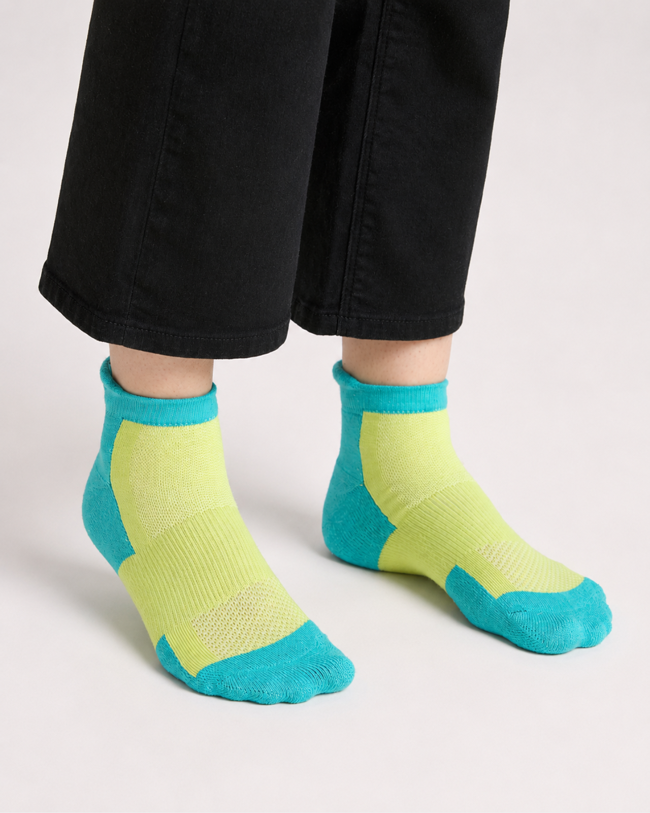 A pair of quarter length technical socks in neon green, worn on a person's feet with black pants.