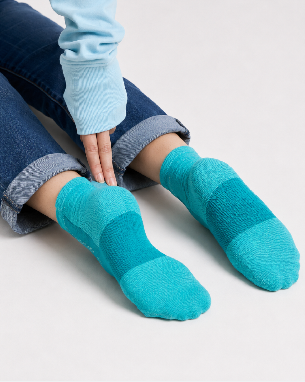 A person sitting cross-legged wearing bright teal and turquoise striped socks with a light blue sweatshirt