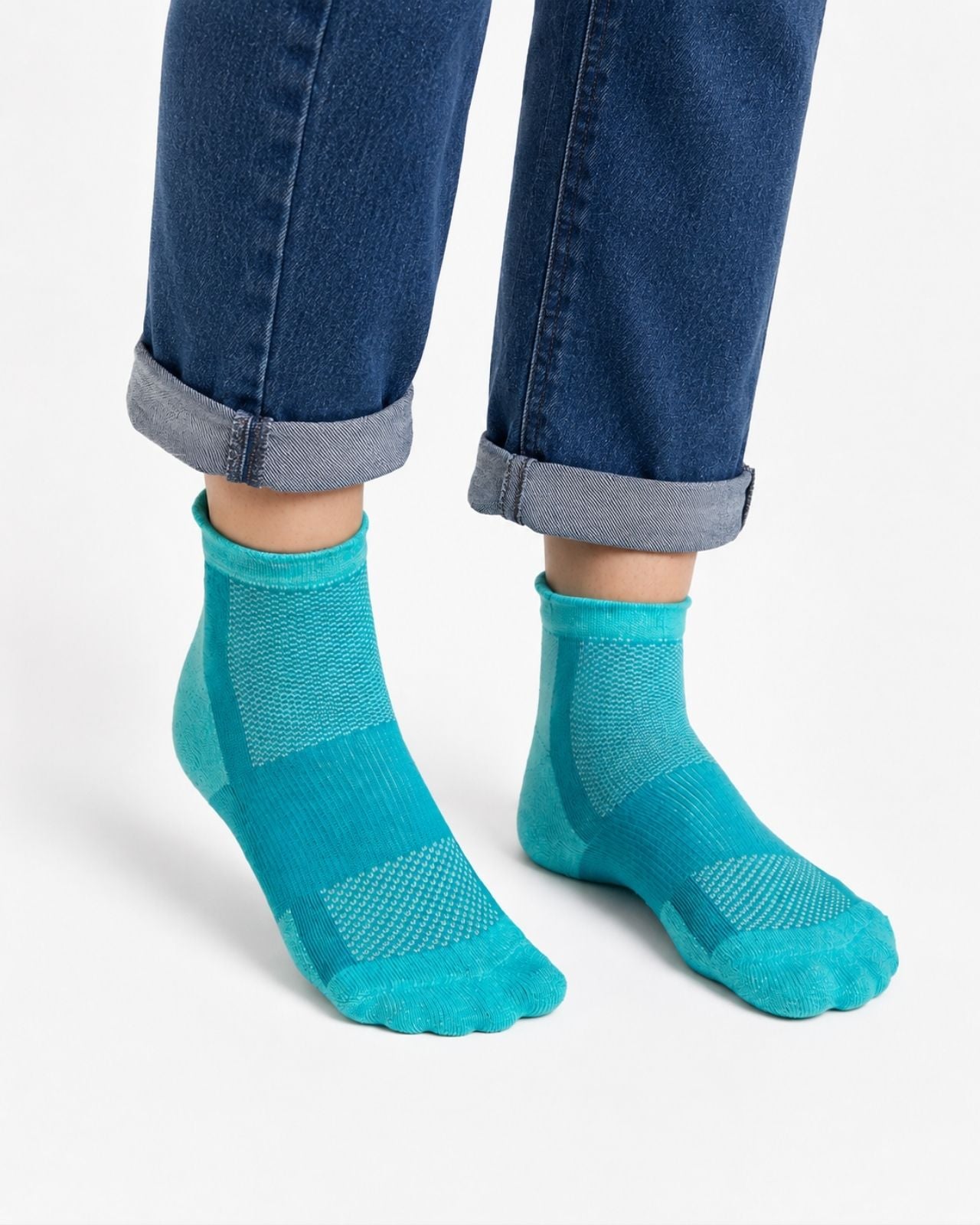 A person wearing teal blue quarter length technical socks with textured knit panels, shown with cuffed blue jeans against a clean white background.